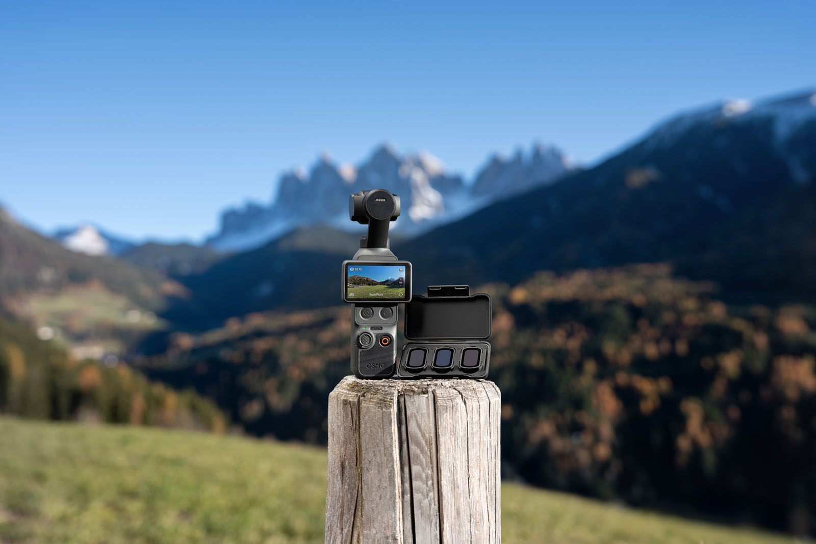 DJI Osmo Pocket 4 mit Zubehör und Filtern auf Holzpfosten, Berglandschaft im Hintergrund