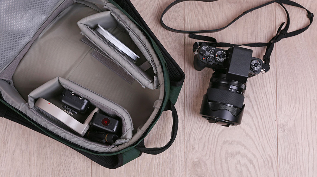 Offene Kameratasche neben Kamera mit Objektiv, Draufsicht auf geordnetes Zubehör und Innenfächer