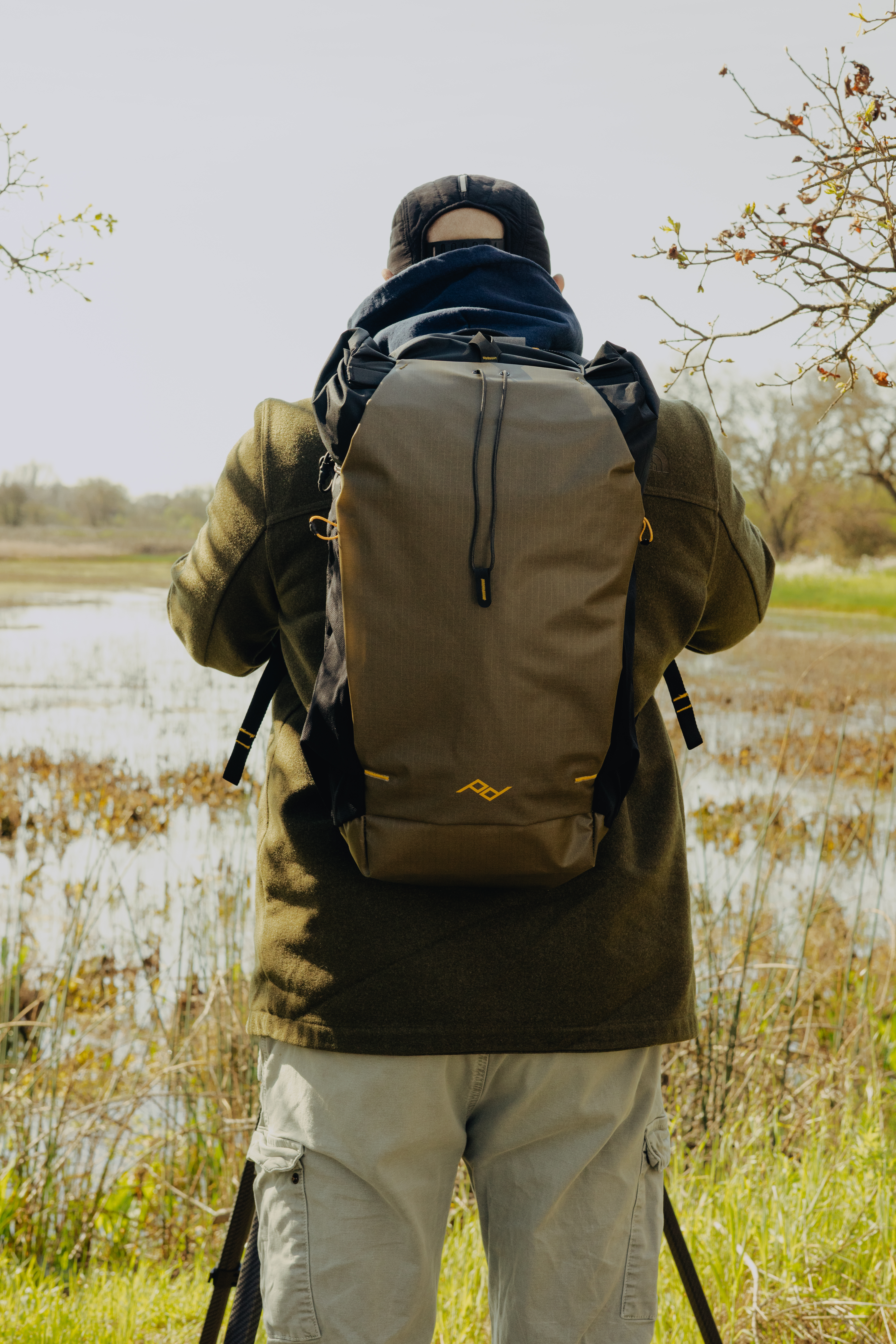 Peak Design Outdoor Backpack 25L (kelp) – getragen im Outdoor-Einsatz am Rücken vor Gewässer und Vegetation