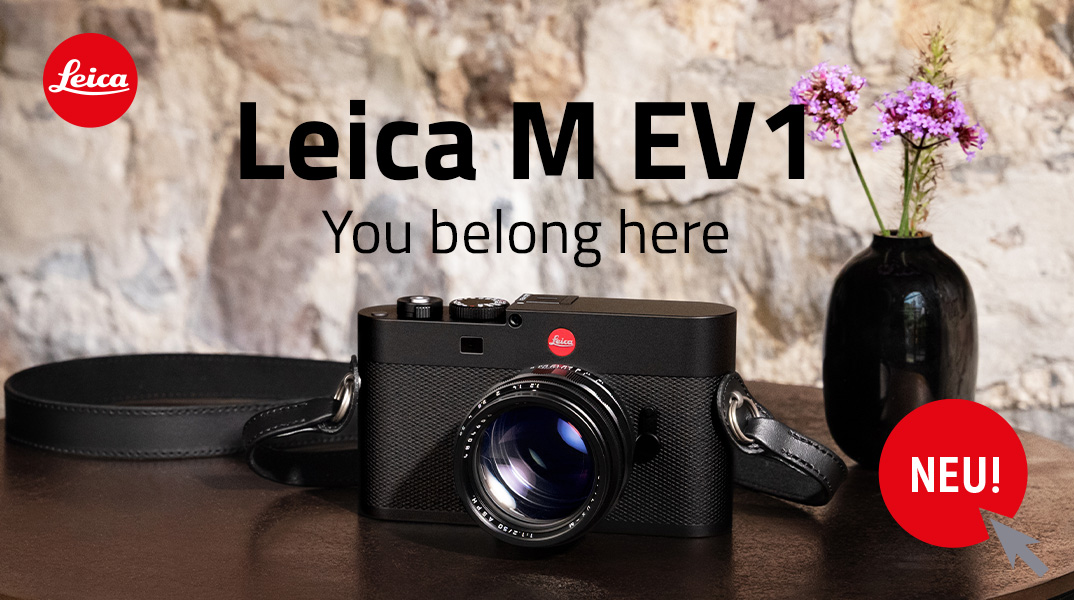 Leica M EV1 auf Holztisch vor Steinwand mit Ledertrageriemen und Vase im Hintergrund, Vorstellung des neuen Modells