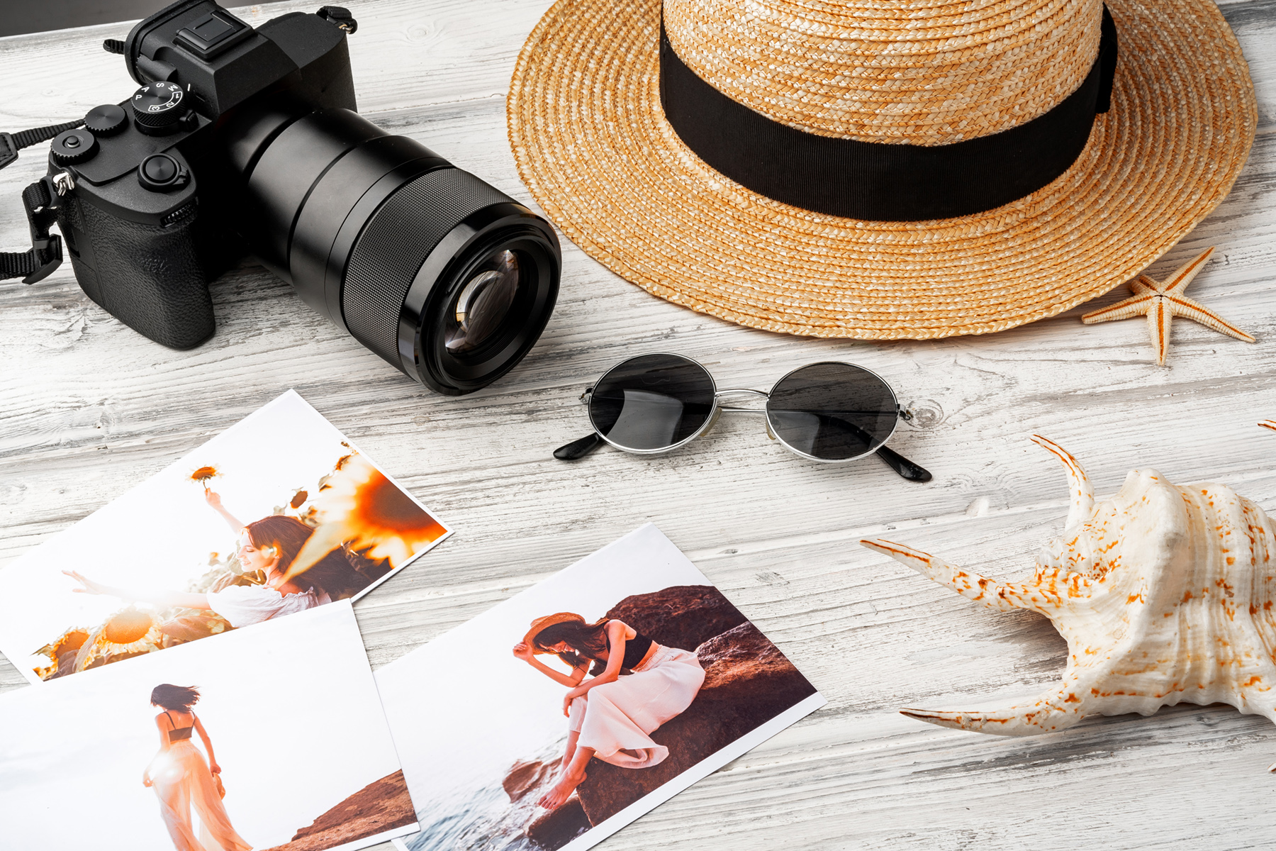 Reisefotografie – Kamera mit Strohhut, Sonnenbrille, Muscheln und Abzügen auf Holztisch