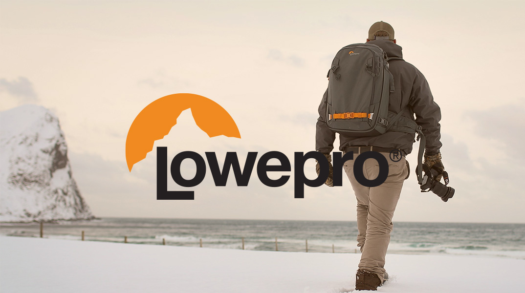 Fotograf mit Lowepro Fotorucksack auf verschneitem Strand, Kamera in der Hand, Blick Richtung Meer und Felsen