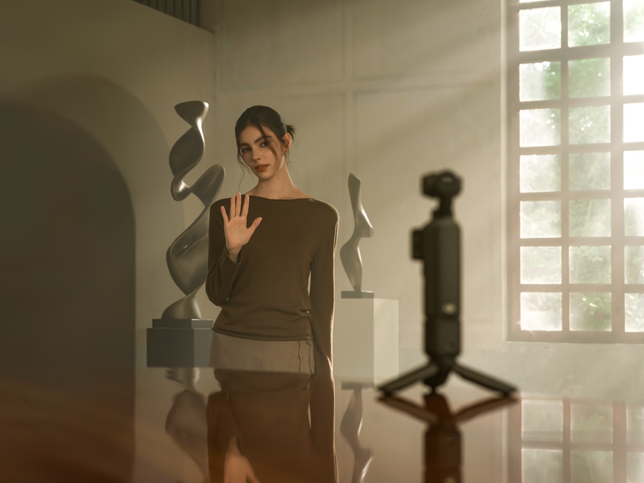 DJI Osmo Pocket 4 – Vorderansicht auf kleinem Stativ mit Person im Hintergrund bei Videoaufnahme im Innenraum