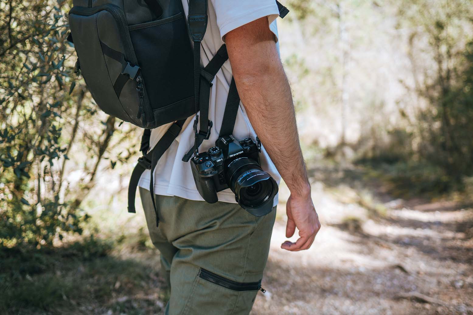 Seitliche Ansicht einer getragenen OM System OM-1 am Körper, kombiniert mit Rucksack beim Wandern
