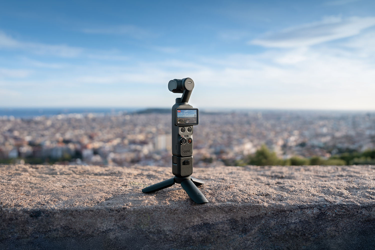 DJI Osmo Pocket 3 auf Mini-Stativ, Vorderansicht mit Stadtpanorama im Hintergrund bei Tageslicht