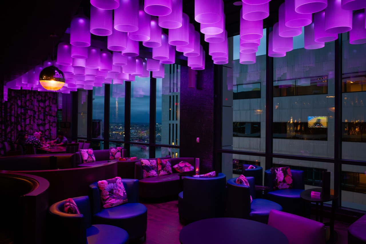 Lounge-Innenraum mit violetter LED-Deckenbeleuchtung, Sitzbereichen und Fensterfront vor der Bearbeitung