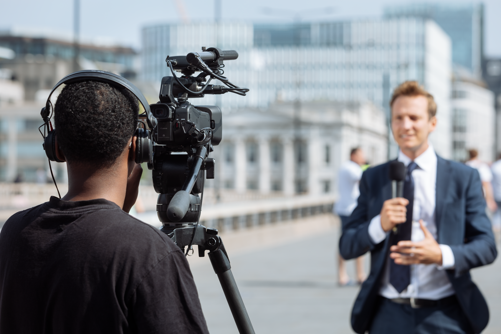 Kamerateam filmt Reporter mit Mikrofon bei Außenaufnahme in urbaner Umgebung