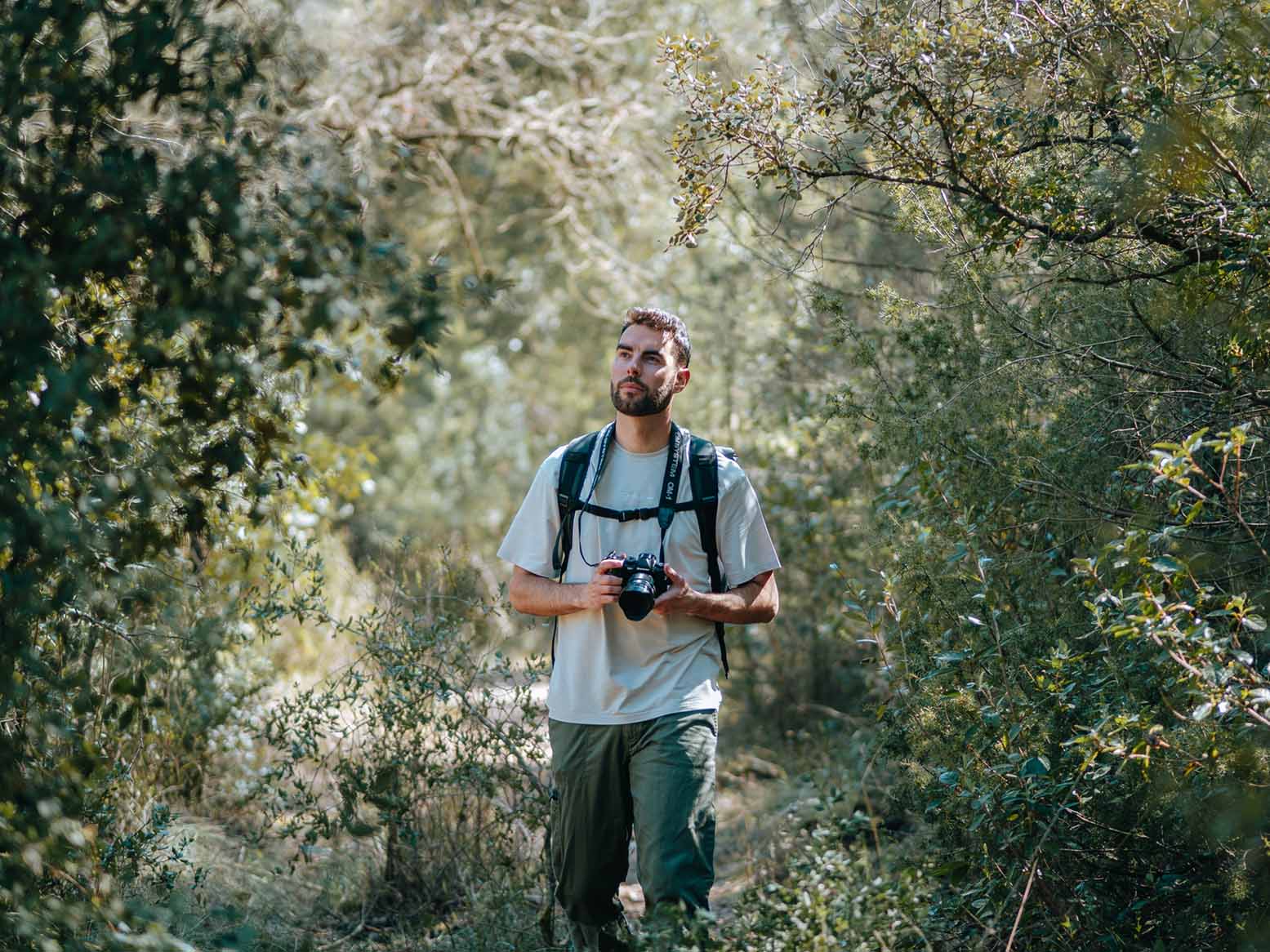 Person mit OM System OM-1 beim Wandern auf schmalem Pfad im Wald, Kamera einsatzbereit in den Händen