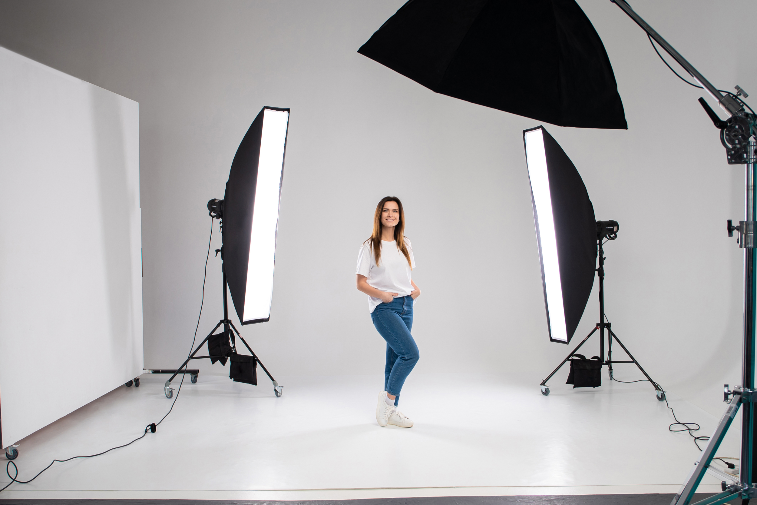 Frau posiert im Fotostudio zwischen Softboxen und professioneller Studiobeleuchtung vor weißem Hintergrund