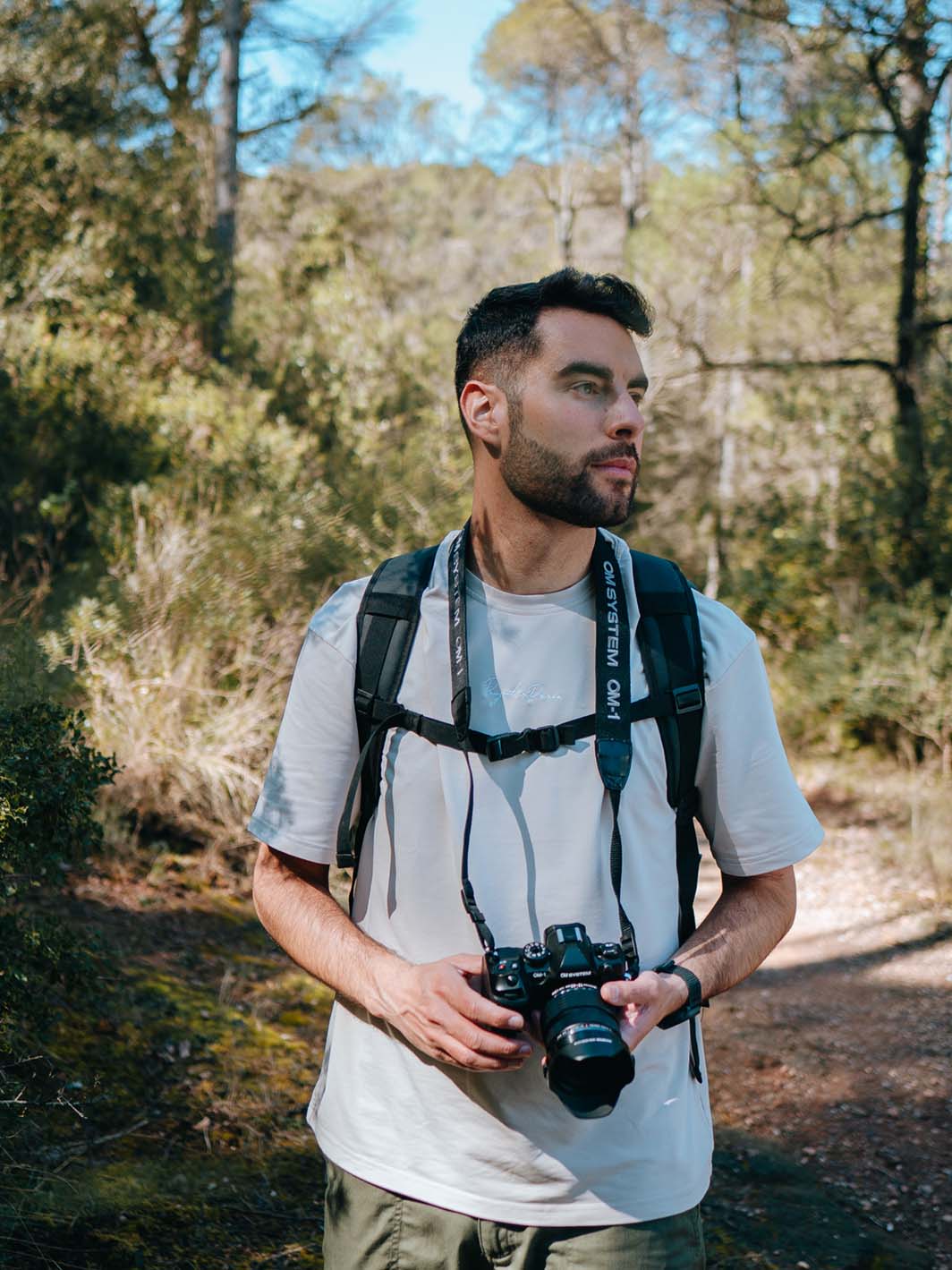 Wanderer mit OM System OM-1 und Rucksack auf Waldweg, Porträtaufnahme im natürlichen Outdoor-Einsatz