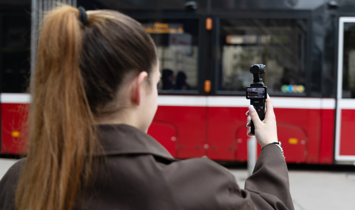 DJI Osmo Pocket 3 in Anwendung, Person filmt Straßenbahn aus Schulterperspektive im urbanen Umfeld