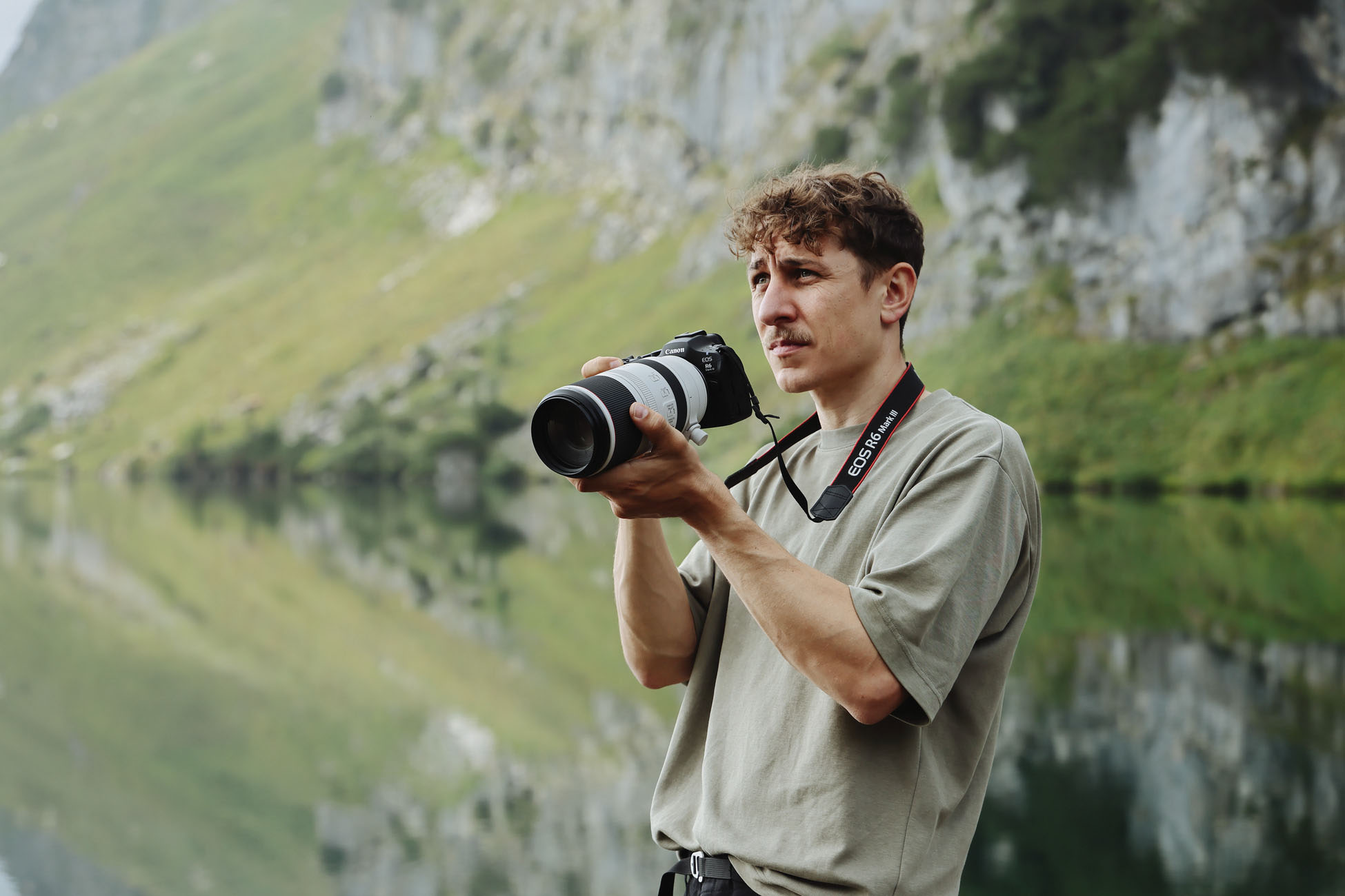 Canon EOS R6 Mark III im Einsatz, Fotograf hält Kamera mit Teleobjektiv vor Berglandschaft am See