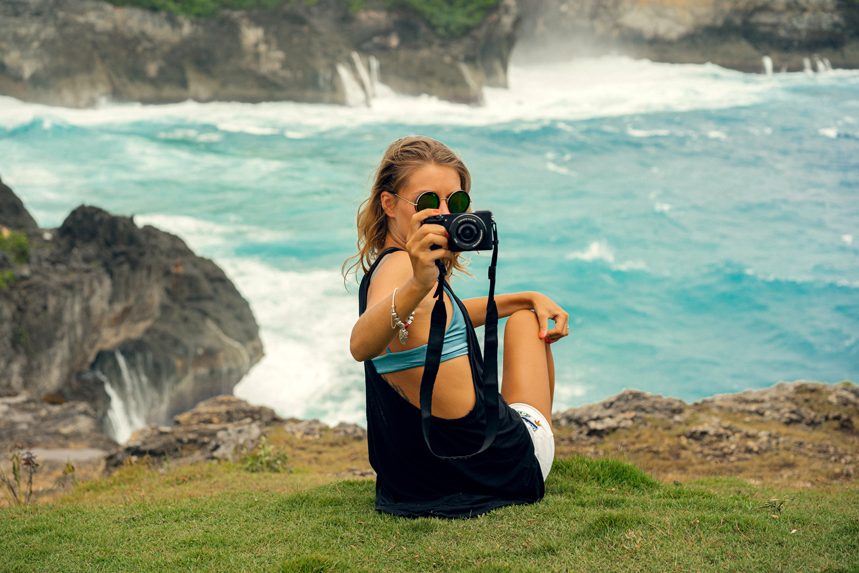 Reisefotografie – Frau mit Kamera sitzt an einer felsigen Küste mit türkisblauem Meer