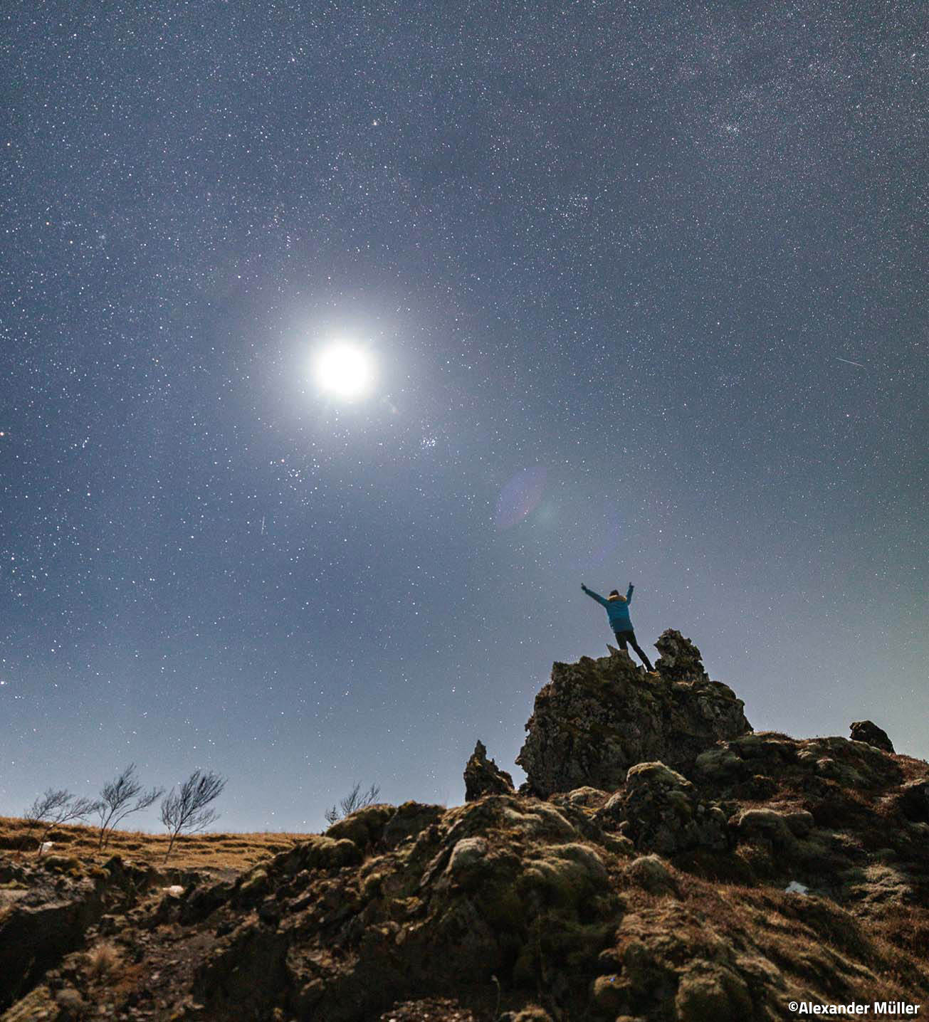 Canon RF 14mm F1.4 – Person steht auf Felsen unter hellem Sternenhimmel und hebt die Arme in die Höhe