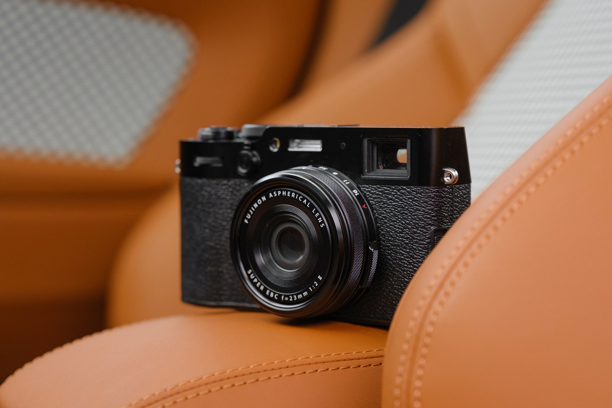 Fujifilm X100VI in Schwarz – Kompaktkamera auf braunem Ledersitz in stilvoller Umgebung