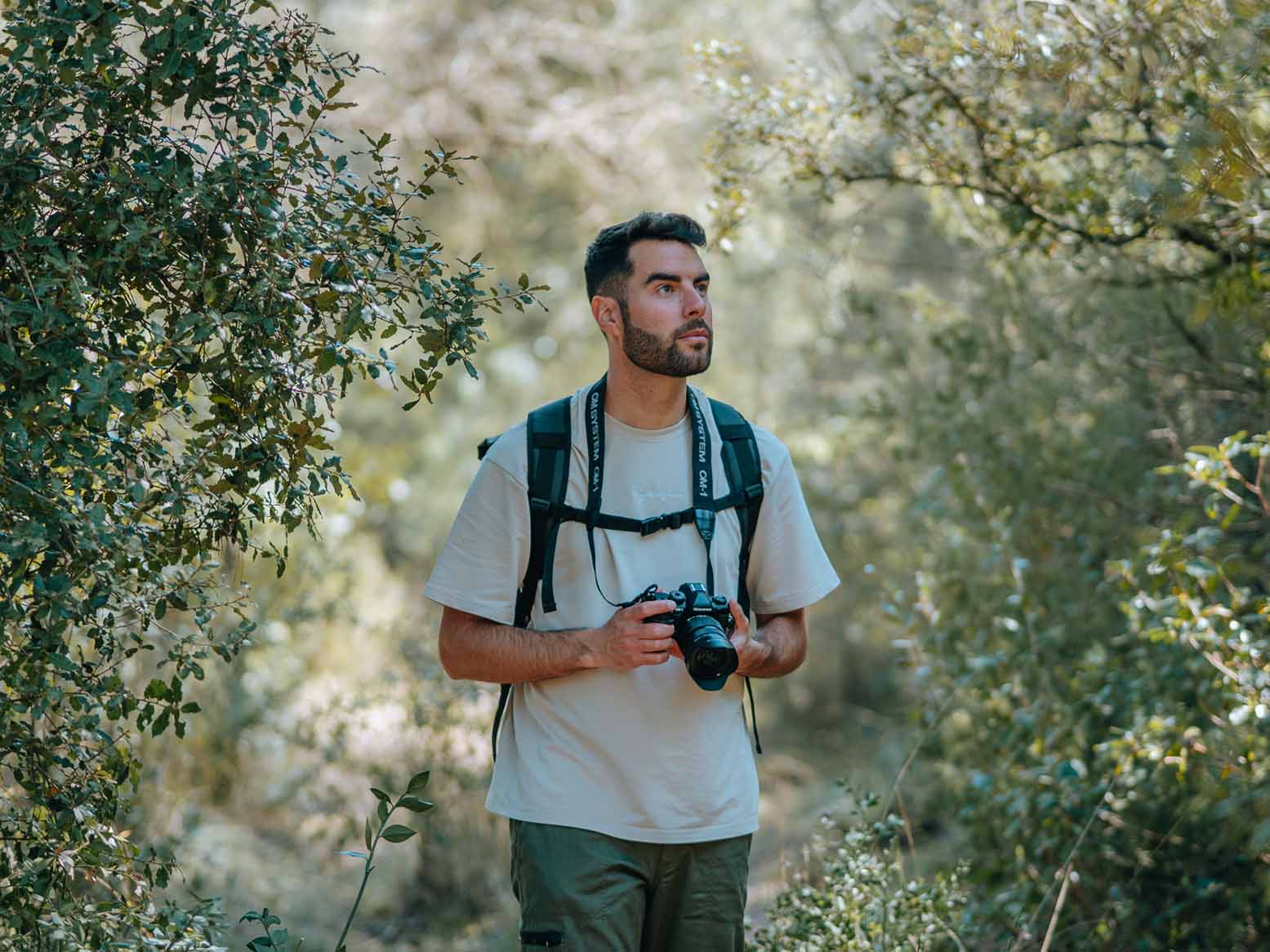 Fotograf mit Rucksack hält OM System Systemkamera in den Händen im Wald, bereit für Outdoor-Aufnahmen