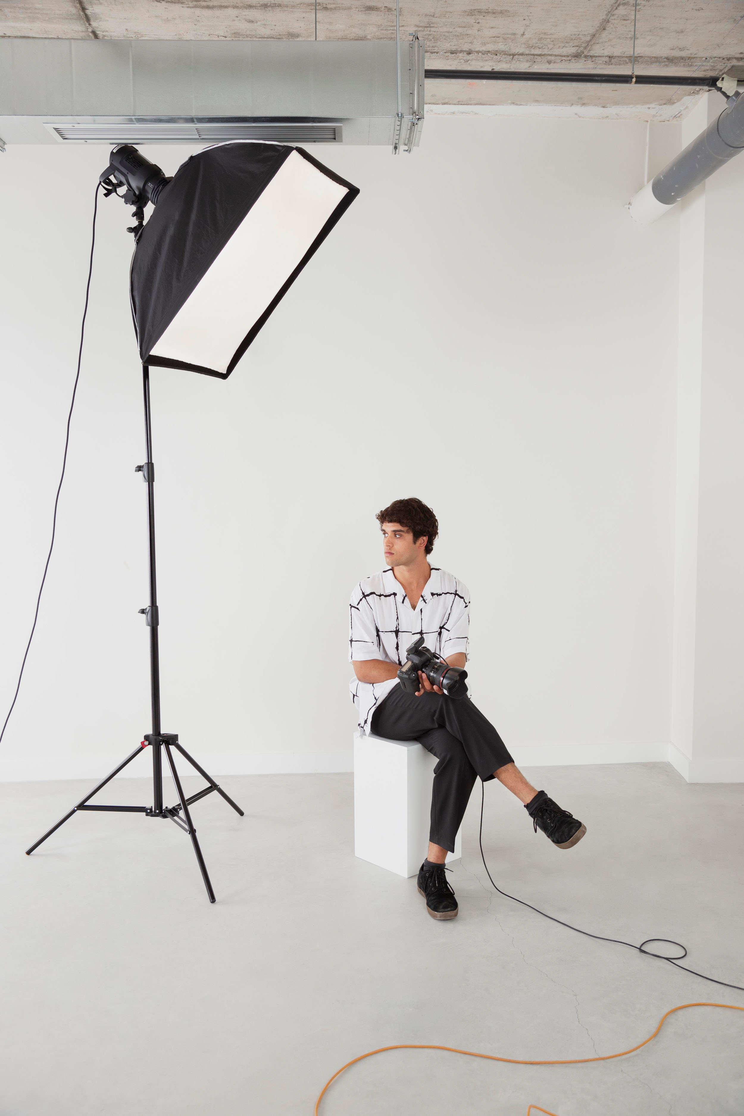 Fotograf sitzt mit Kamera neben großer Softbox in minimalistischem Fotostudio